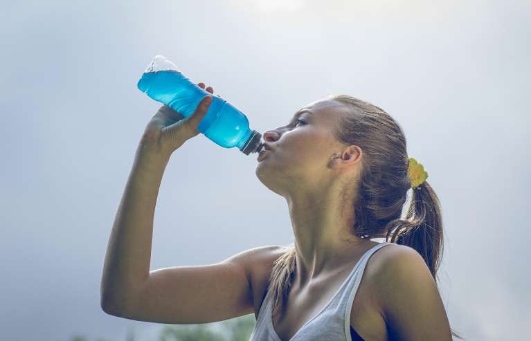 Young woman drinking from a blue sports bottle outdoors, representing hydration and how different wa
