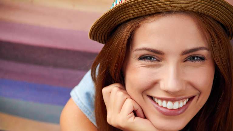 Smiling woman with bright white teeth wearing a hat, showcasing healthy dental care results at a Pon