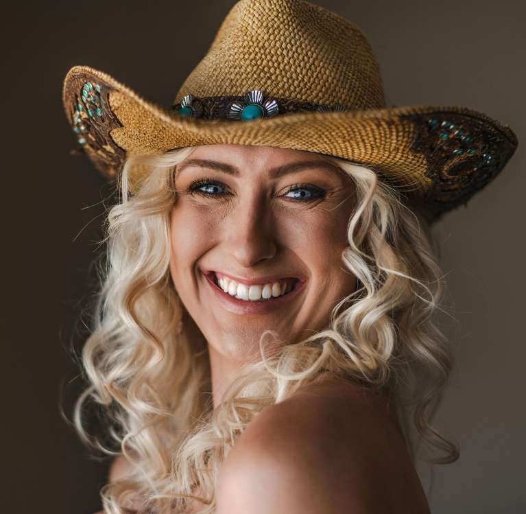 Smiling woman with curly blonde hair wearing a decorative cowboy hat
