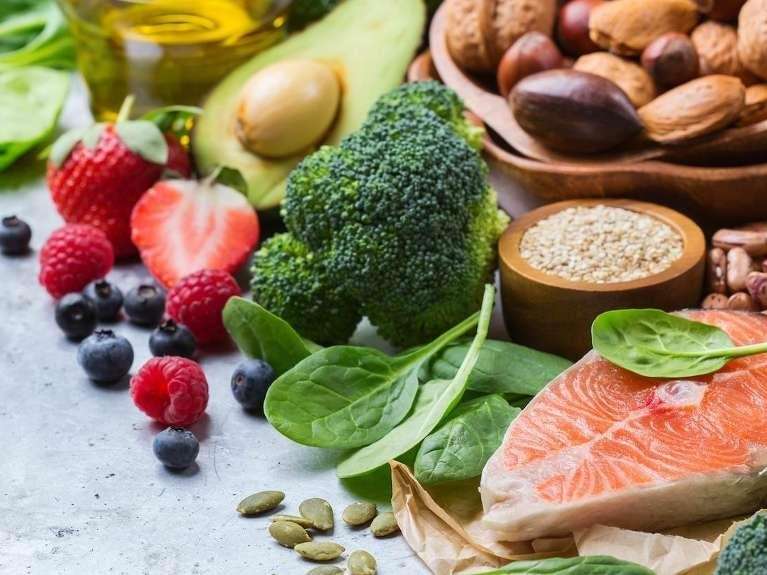 Fresh assortment of healthy foods including salmon, avocado, broccoli, spinach, berries, nuts, and s