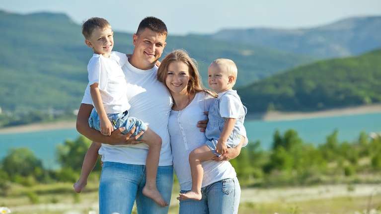 mother, father, and two young sons smiling near a lake in Coeur d'Alene